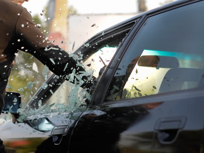 Eingeschlagene Seitenscheibe Jemand schlägt die Scheibe eines schwarzen Autos ein.